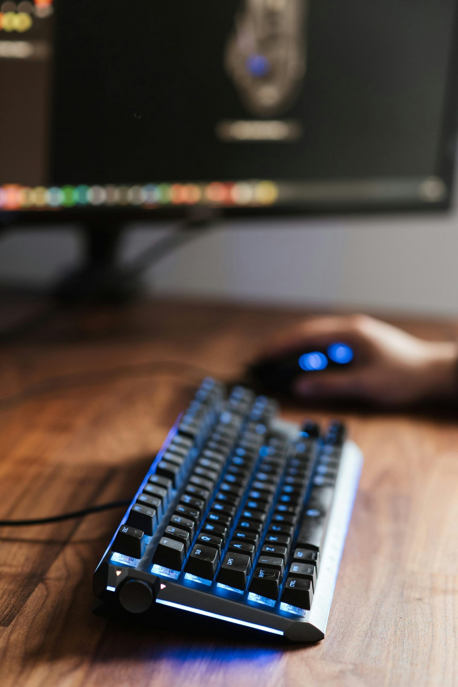 Home Crop unrecognizable person sitting at table with computer monitor and backlit keyboard while using mouse at home